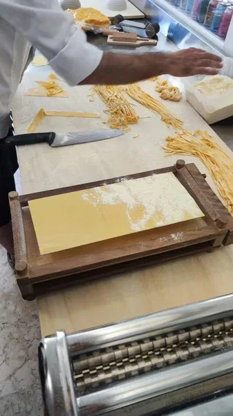 Preparazione artigianale di pasta fresca emiliana su banco da lavoro, con tagliatelle e sfoglia.