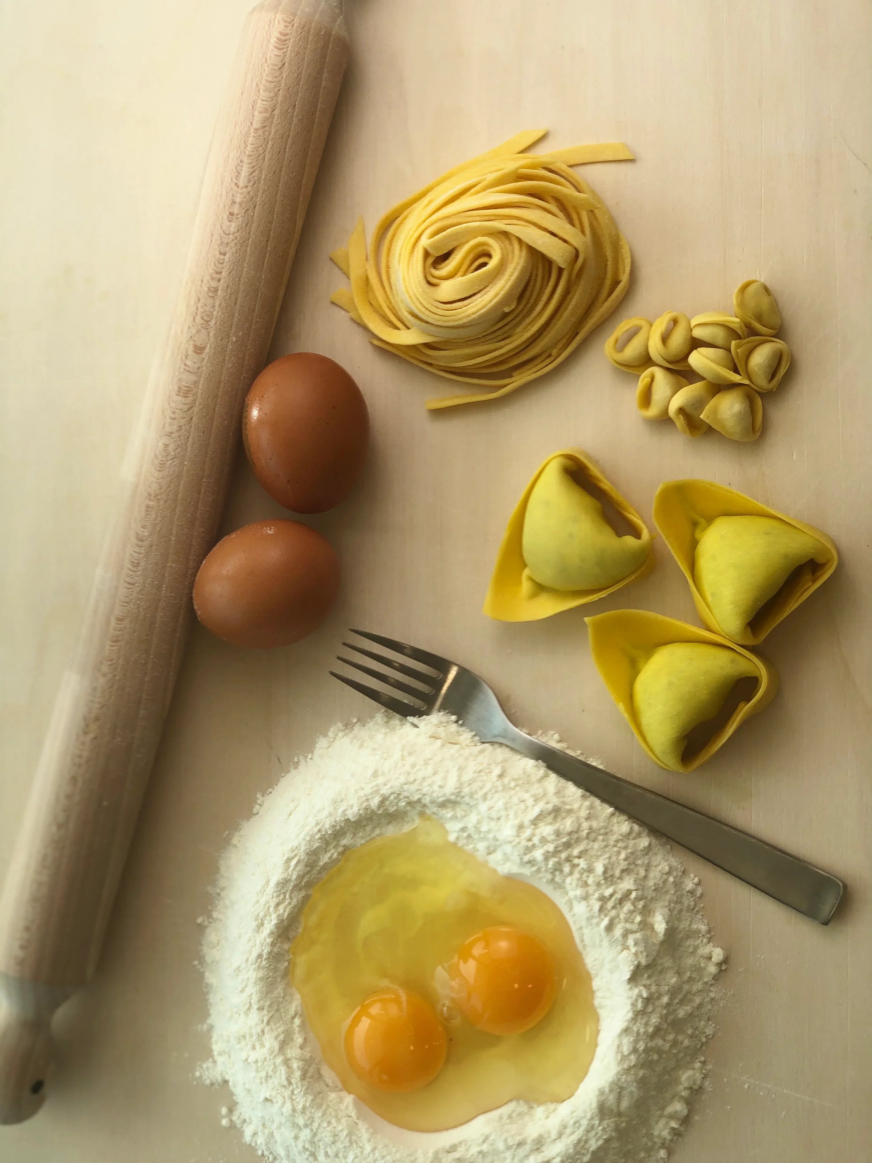 Ingredienti per pasta fresca emiliana con uova, farina, mattarello, tagliatelle, tortellini e tortelloni.