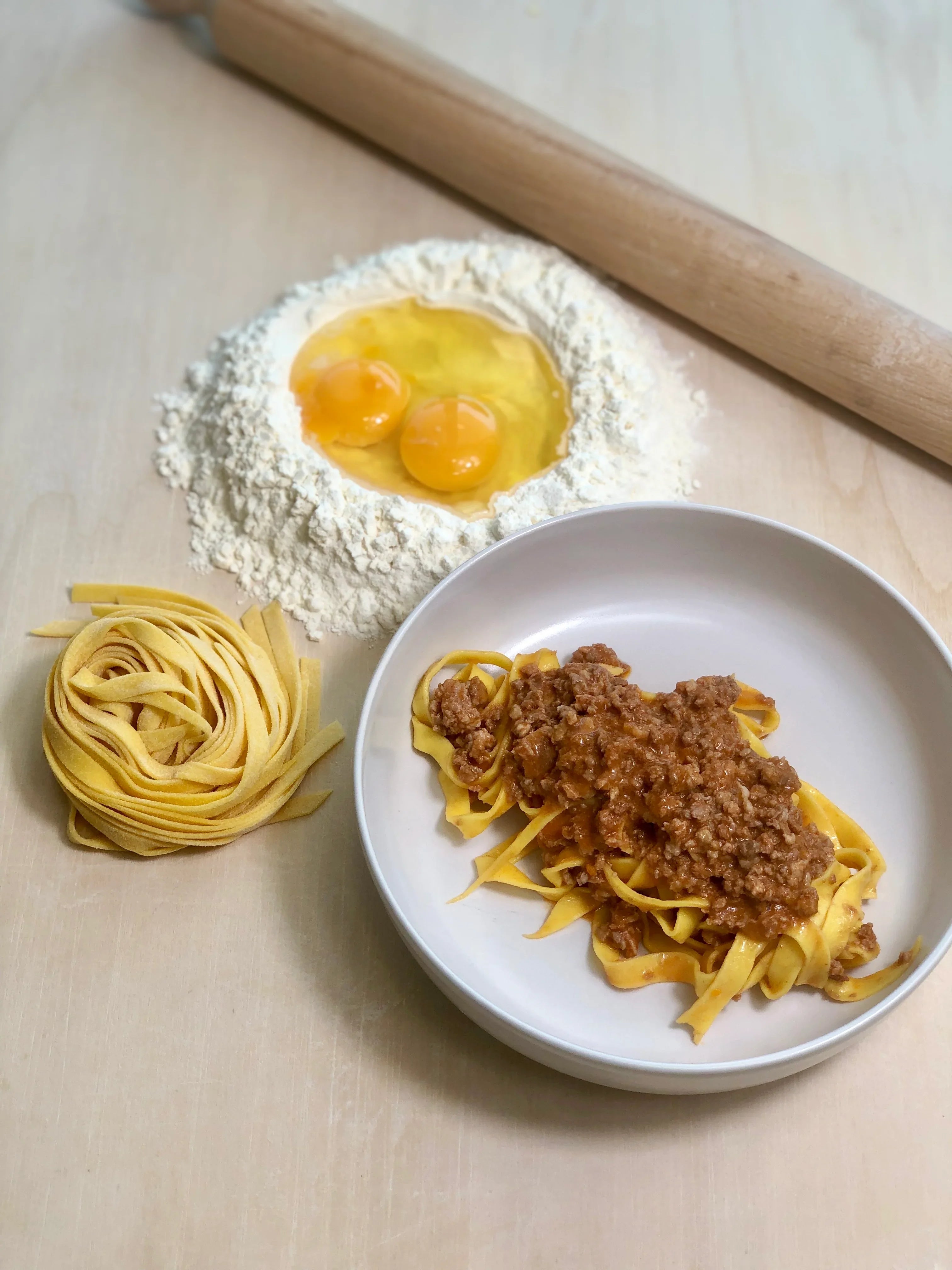 Tagliatelle fresche con ragù alla bolognese, farina e uova su tavolo da cucina artigianale