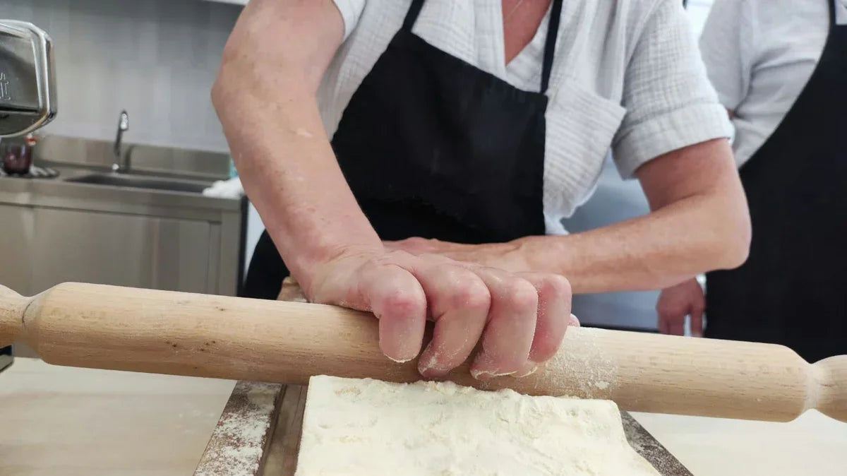 Mani che stendono pasta fresca artigianale con mattarello durante corso di cucina emiliana