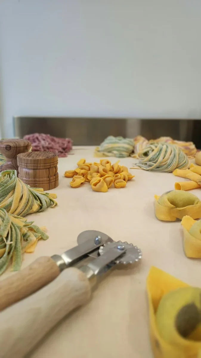 Pasta fresca artigianale emiliana assortita su tavolo di lavoro, con utensili da cucina.