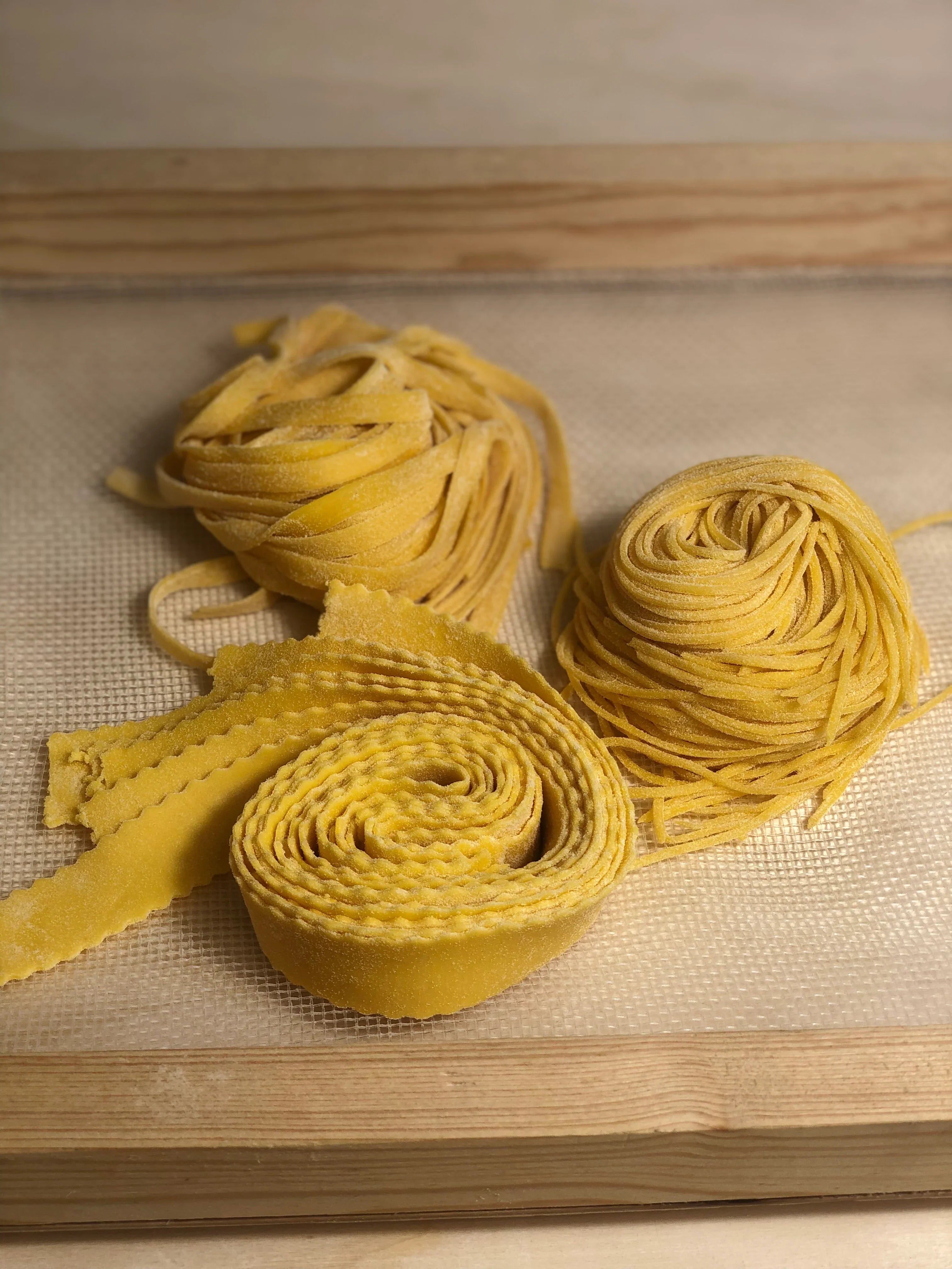 Tagliatelle, tagliolini e pappardelle fresche artigianali disposte su vassoio di legno